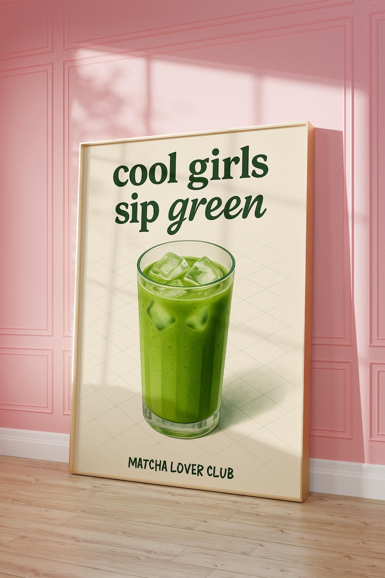 May include: A framed poster featuring the words "cool girls sip green" above a glass of green drink with ice cubes. The text "Matcha Lover Club" is at the bottom. The poster is propped against a pink wall.