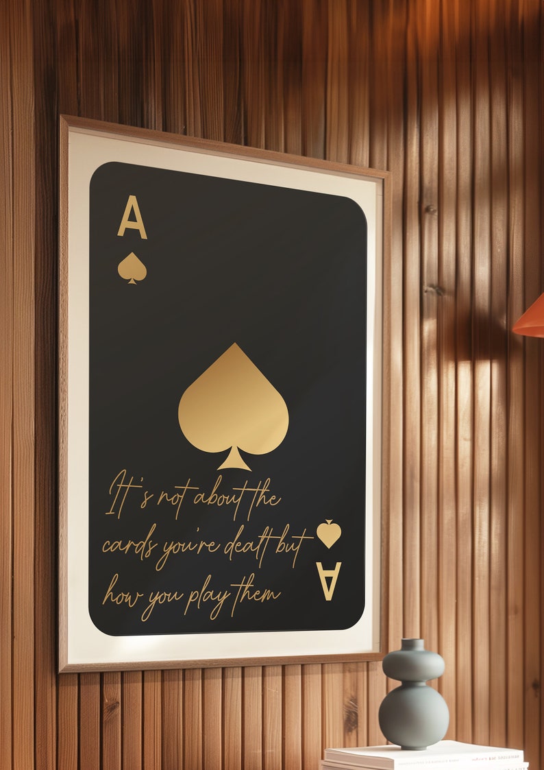 Pode incluir: Um p&ocirc;ster preto e dourado emoldurado com um &aacute;s de paus dourado de baralho e o texto "N&atilde;o se trata das cartas que voc&ecirc; recebe, mas de como voc&ecirc; as joga."