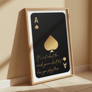 Pode incluir: Uma impress&atilde;o emoldurada preta e dourada com um design de carta de jogo de &aacute;s de paus dourado. O texto na impress&atilde;o diz "N&atilde;o se trata das cartas que voc&ecirc; recebe, mas de como voc&ecirc; as joga."