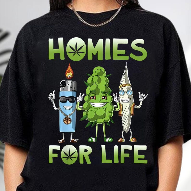 A black t-shirt with a graphic design featuring three anthropomorphic objects: a lighter, a grape, and a surfboard, along with the text "HOMIES FOR LIFE".