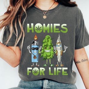 A person wearing a gray t-shirt with a graphic design featuring three cartoon-like characters and the text "HOMIES FOR LIFE".
