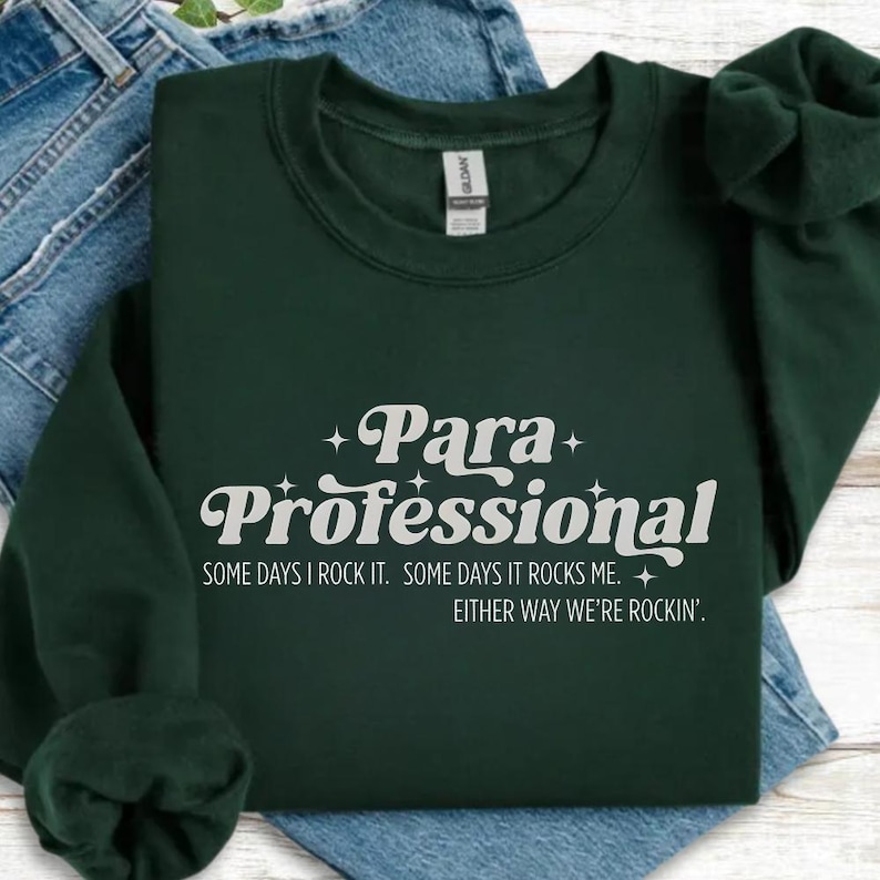 A green sweatshirt with white text printed on it, placed on top of a pair of blue jeans.