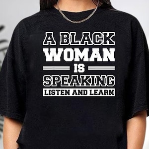 May include: Black sweatshirt with the text "A BLACK WOMAN IS SPEAKING LISTEN AND LEARN" in white block letters. The text is centered on the chest of the shirt. The shirt has a crew neck and long sleeves.
