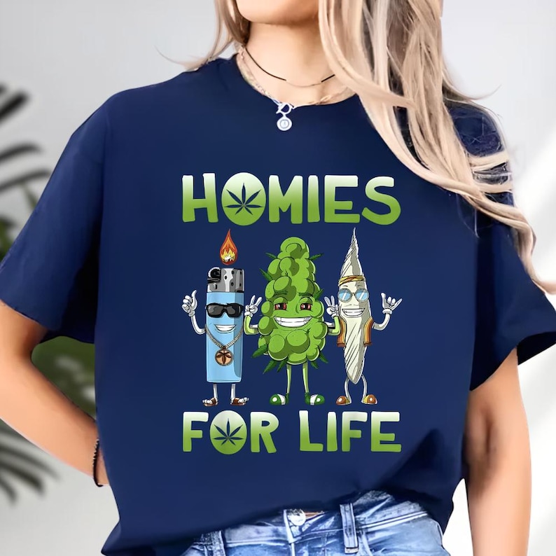 A blue t-shirt with a graphic design featuring three cartoon-style objects, including a lighter, a bud, and a leaf, along with the text "HOMIES FOR LIFE".