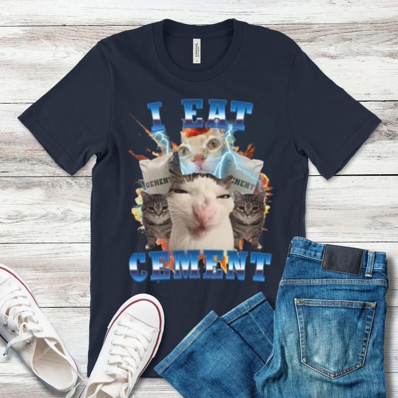 A black t-shirt with a graphic design featuring a cat and the text "I EAT CEMENT" in a playful, humorous manner.