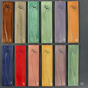 May include: Twelve ceramic tiles with a raised design of a flower. The tiles are arranged in two rows of six, and each tile is numbered 1 through 12. The tiles are in various colors, including brown, green, blue, red, pink, yellow, and purple.