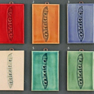May include: Six ceramic tiles with a raised image of a pea pod in various colors: red, orange, blue, white, teal, and green.