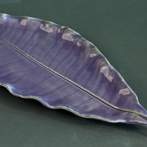 May include: A ceramic leaf-shaped serving dish with a purple glaze. The dish has a realistic leaf design with veins and a slightly wavy edge.