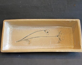 May include: A rectangular, beige ceramic tray with a floral design. The tray has a raised rim and a matte finish. A black, stylized botanical illustration is centered on the tray.