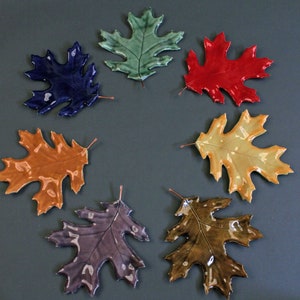 May include: Seven ceramic oak leaves in different colors, including blue, green, red, orange, yellow, purple, and brown. The leaves are arranged in a circle on a gray background.