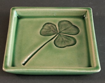 May include: A green ceramic square dish with a raised four-leaf clover design.