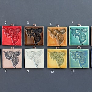 May include: Twelve ceramic tiles with a bee design in various colors, including green, red, brown, yellow, blue, and white. Each tile has a copper hanger.
