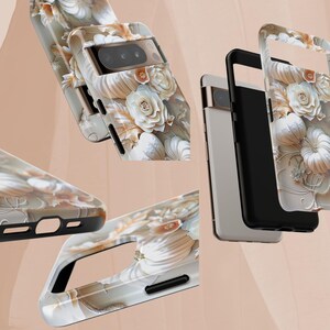 May include: Phone cases with a floral design. The cases feature a pattern of white roses and other flowers on a light beige background. The cases have black edges and cutouts for the camera and other phone features.