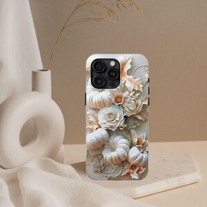 May include: A white iPhone case with a 3D floral design. The case features pumpkins and roses in white and peach tones. The case has a glossy finish and a black camera module.