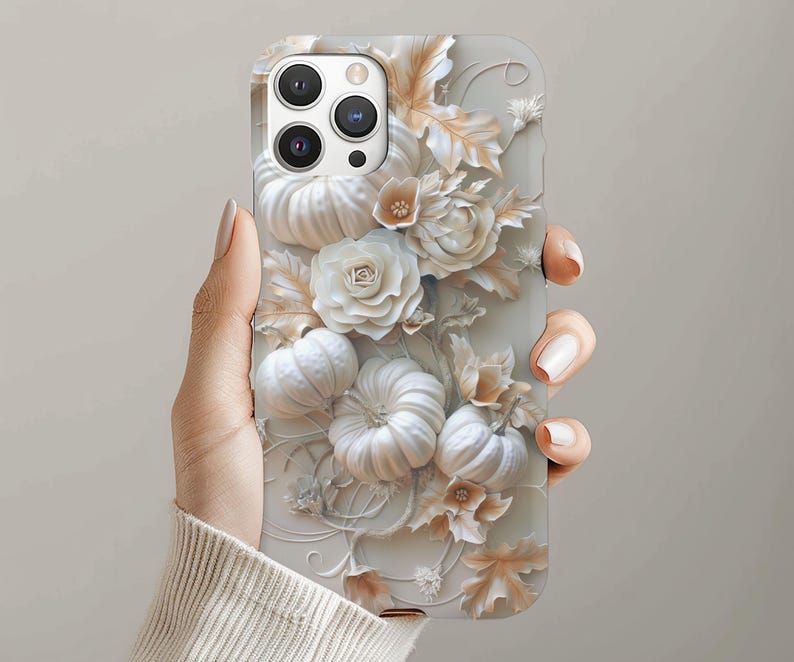 May include: A phone case with a 3D design of white pumpkins, roses, and leaves. The case has a light grey background and a textured appearance. The design includes intricate details and a seasonal autumn theme.