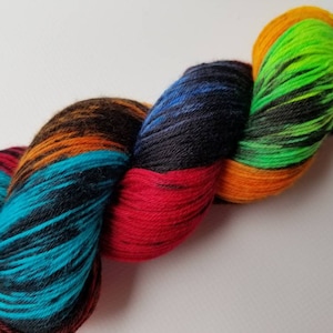 May include: A close-up of a skein of colorful yarn. The yarn is a mix of vibrant colors, including red, teal, black, orange, green, yellow, and blue. The yarn is twisted and appears soft, ideal for knitting or crocheting projects.