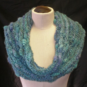 May include: A teal and blue knitted infinity scarf with a textured, bumpy design.