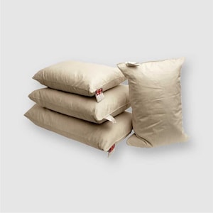 May include: Four cream-coloured pillows stacked on top of each other. The pillows are made of a soft, natural fabric and have a simple, elegant design.