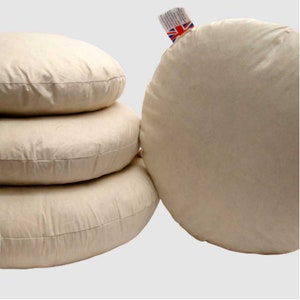 May include: Four round, white cotton cushions stacked on top of each other. The cushions are all the same size and shape.
