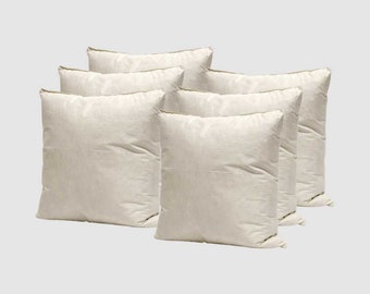 May include: Six off-white square throw pillows with a subtle texture. The pillows are arranged in a staggered pattern.