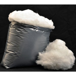 May include: A large bag of white polyester fibrefill stuffing for crafts, pillows, and other projects. The bag is grey and has a drawstring closure. There is a smaller pile of fibrefill next to the bag.