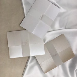 May include: Three folded white and cream paper envelopes with a translucent vellum overlay. The vellum overlays have handwritten calligraphy in black ink.