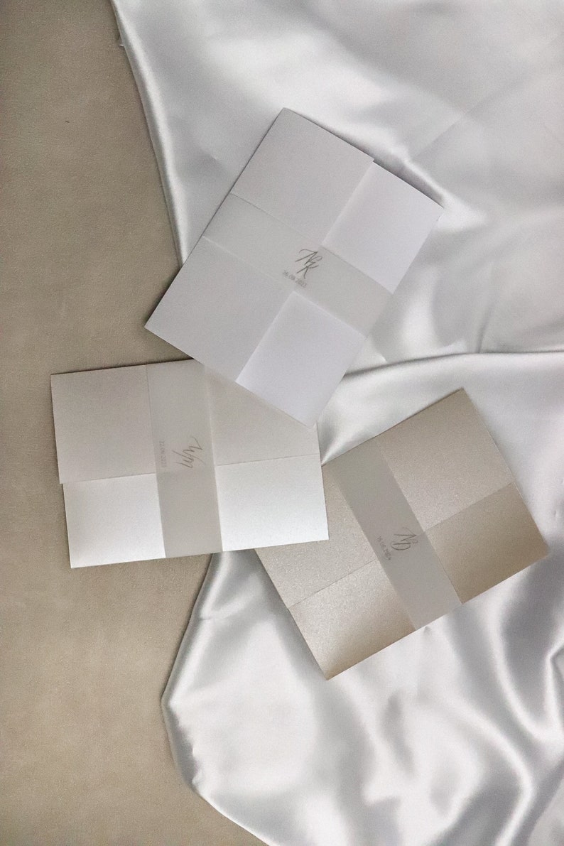 May include: Three folded white and cream paper envelopes with a translucent vellum overlay. The vellum overlays have handwritten calligraphy in black ink.