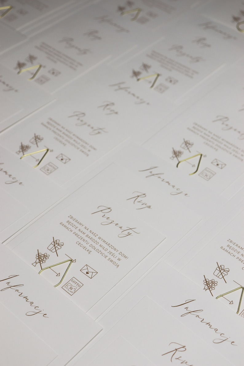 May include: A set of white cards with gold lettering and illustrations. The cards have the words "Prezenty" and "Informacje" on them. The illustrations are of a gift box, a house, and a letter.