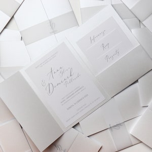 May include: A white wedding invitation with a gray envelope. The invitation features the names "Anna & Dominik" in cursive script. The envelope has three pockets labeled "Information", "RSVP", and "Presents".