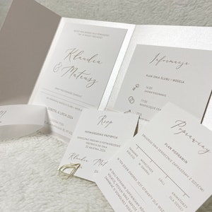 May include: A wedding invitation suite with a white background and gold accents. The invitation features the names "Klaudia & Mateusz" in a script font. The RSVP card includes the text "Potwierdzenie Przybycia" and the date "30 Kwietnia 2024". The information card includes a schedule for the wedding day, with times for the ceremony, reception, and after-party. The invitation also includes a map of the venue.