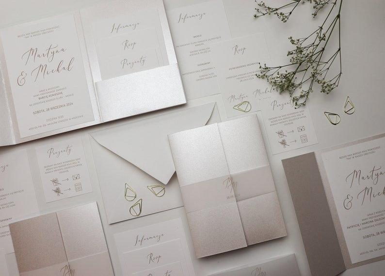 May include: A set of wedding invitations with a modern, minimalist design. The invitations are printed on white cardstock with gold foil accents. The text on the invitations includes the names "Martyna & Michal" and the date "SOBOTA, 28 WRZESNIA 2014".