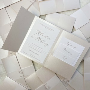 May include: A white wedding invitation with a pocket for RSVP cards. The invitation features the names "Klaudia & Mateusz" in elegant calligraphy and the date "SOBOTA, 6 LIPCA 2024".