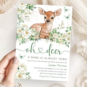 Könnte beinhalten: Babyparty-Einladung mit einem Reh, weißen Blumen und grünem Laub. Der Text "oh deer" ist in grüner Schrift geschrieben, zusammen mit den Veranstaltungsdetails. Schmetterlinge ergänzen das Design.