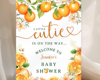 May include: A baby shower welcome sign featuring watercolor oranges, blossoms, and green leaves. The sign reads "A little cutie is on the way... Welcome to Jennifer's Baby Shower."