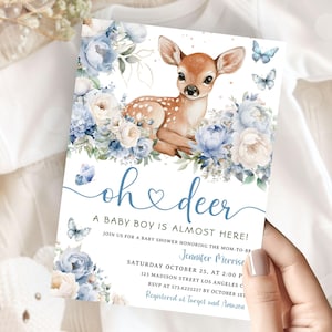 Könnte beinhalten: Babyparty-Einladung mit einem Reh, blauen Blumen und Schmetterlingen. Der Text lautet "oh deer, A baby boy is almost here!" mit Veranstaltungsdetails. Die Einladung wird von einer Person gehalten.