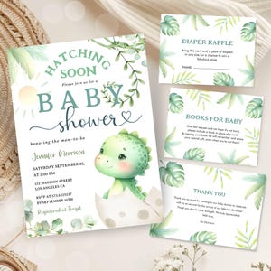 Può includere: Un invito a un baby shower con un dinosauro verde che esce da un uovo. L'invito include il testo "Hatching Soon" e "Please join us for a Baby Shower".