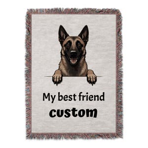 Op de afbeelding: Geweven sprei met een illustratie van een lachende Belgische Mechelse herder. De kop en poten van de hond zijn zichtbaar boven een witte lijn, met de tekst "My best friend custom" eronder. De deken heeft een gefranjerde rand.