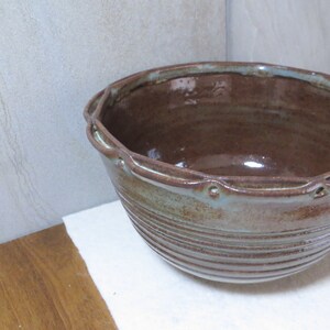 May include: A large brown and blue ceramic bowl with a decorative rim and a glazed finish. The bowl has a rustic look and is perfect for serving salads, soups, or other dishes.