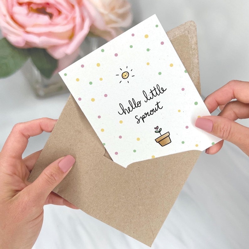 Peut inclure: Une carte de v&oelig;ux avec un fond de pois de couleur vert clair, jaune et rose. La carte dit "hello little sprout" avec un soleil et une plante en pot avec une feuille en forme de c&oelig;ur.
