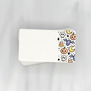 May include: A stack of white note cards with a Halloween themed border. The border features a black bat, a skull, a crescent moon, a pumpkin, and candy corn.
