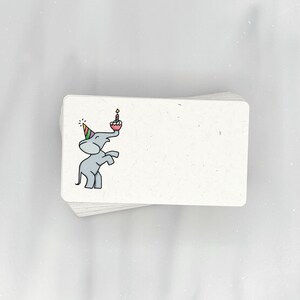 May include: A stack of blank white note cards with a cute cartoon elephant wearing a party hat and holding a birthday cake with a candle on top.