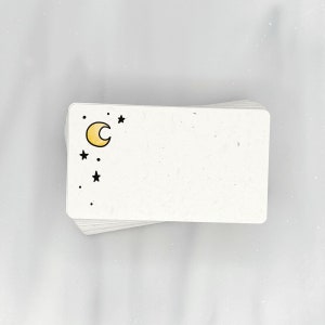 May include: A stack of blank white note cards with a simple black and yellow moon and stars design on the front.