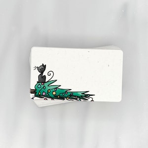 May include: A stack of blank white cards with a black cat sitting on a green Christmas tree with colorful lights. The cat is looking to the left.