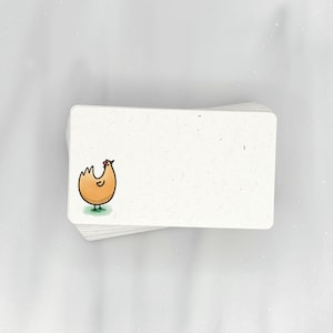May include: A stack of blank white note cards with a hand-drawn illustration of a yellow chicken on the top card.
