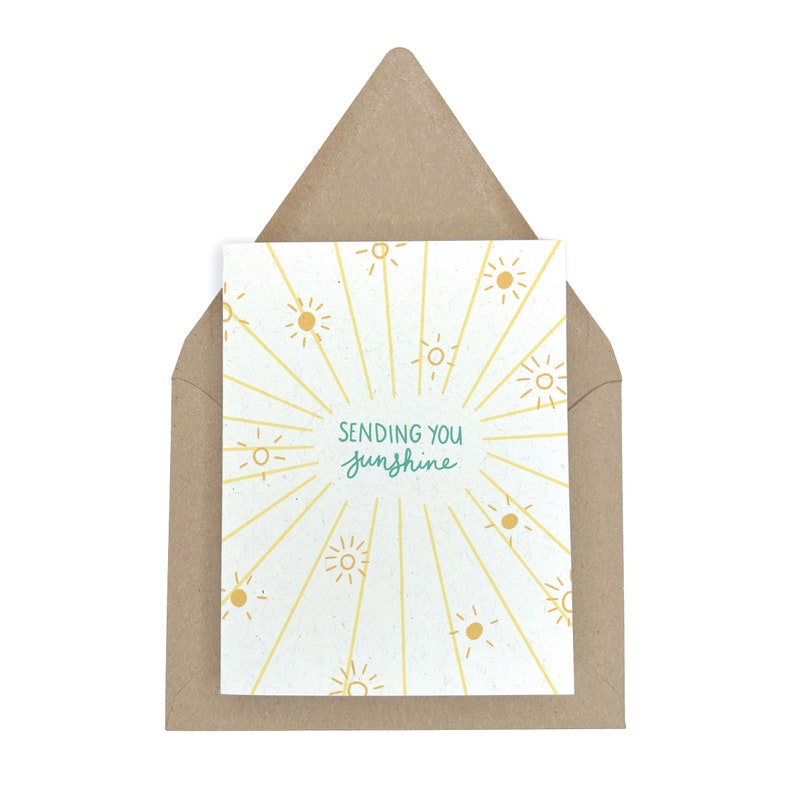 May include: A greeting card with a white background and yellow sun illustrations. The text on the card reads "Sending you sunshine."