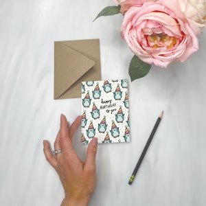 May include: A birthday card with a pattern of cartoon penguins wearing party hats. The card reads "happy BIRTHDAY to you" in black script. A kraft paper envelope, a pencil, and pink roses are also in the image.