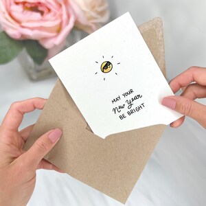 May include: A white card with a yellow sun wearing sunglasses and the text "May your New Year be bright". The card is in a brown envelope.