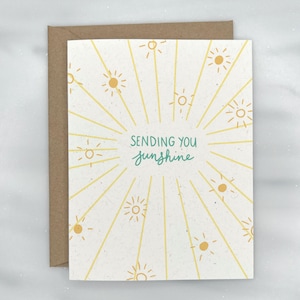 May include: A white card with a yellow sunburst design and the text "Sending you sunshine" in green lettering.