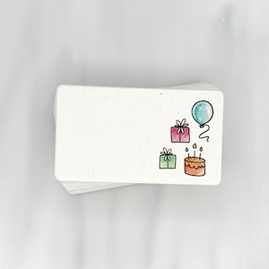 May include: A white card with a birthday theme. The card has a blue balloon, two presents, and a birthday cake with candles.