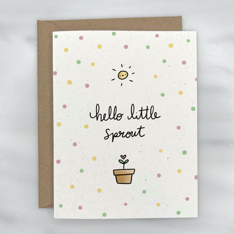 Peut inclure: Une carte blanche avec une enveloppe brun clair. La carte a un fond brun clair avec un motif de petits points jaunes, roses et verts. La carte a un soleil dessin&eacute; &agrave; la main avec un visage souriant, une plante dans un pot et le texte "hello little sprout".